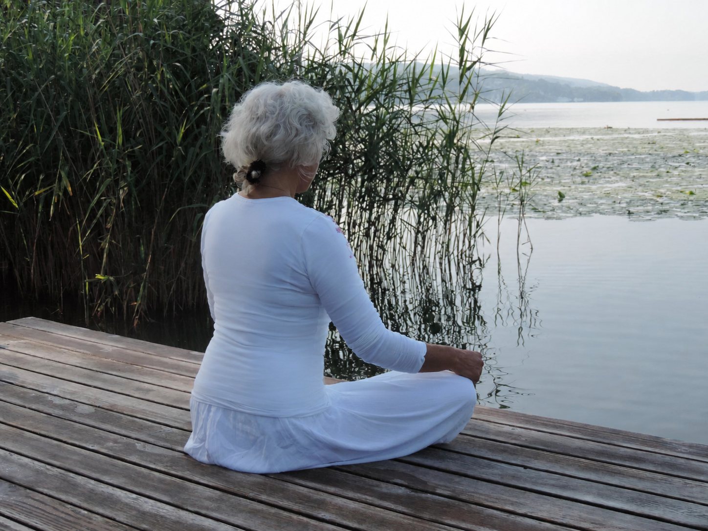 Diana Thommen sitzt in Meditation auf einem Holzsteg am Hallwilersee