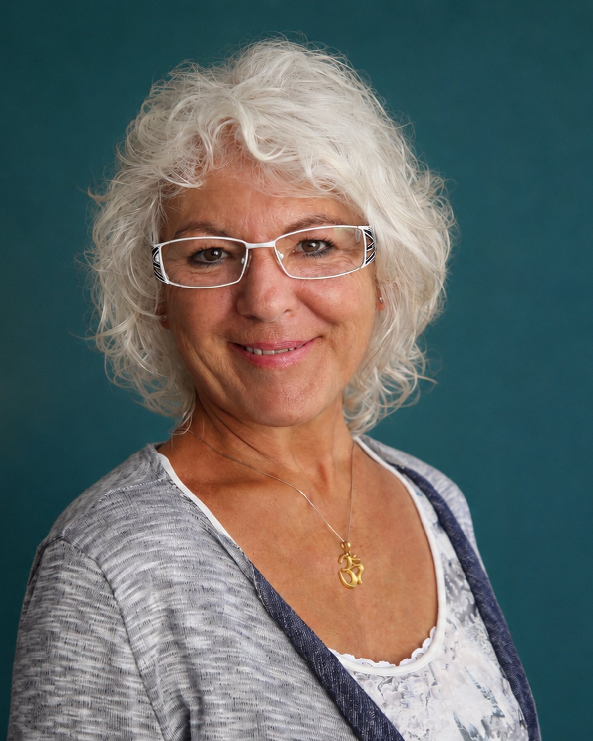 Diana Thommen im Porträt vor einer petrolfarbenen Wand, mit Om-Anhänger an einer feinen Kette