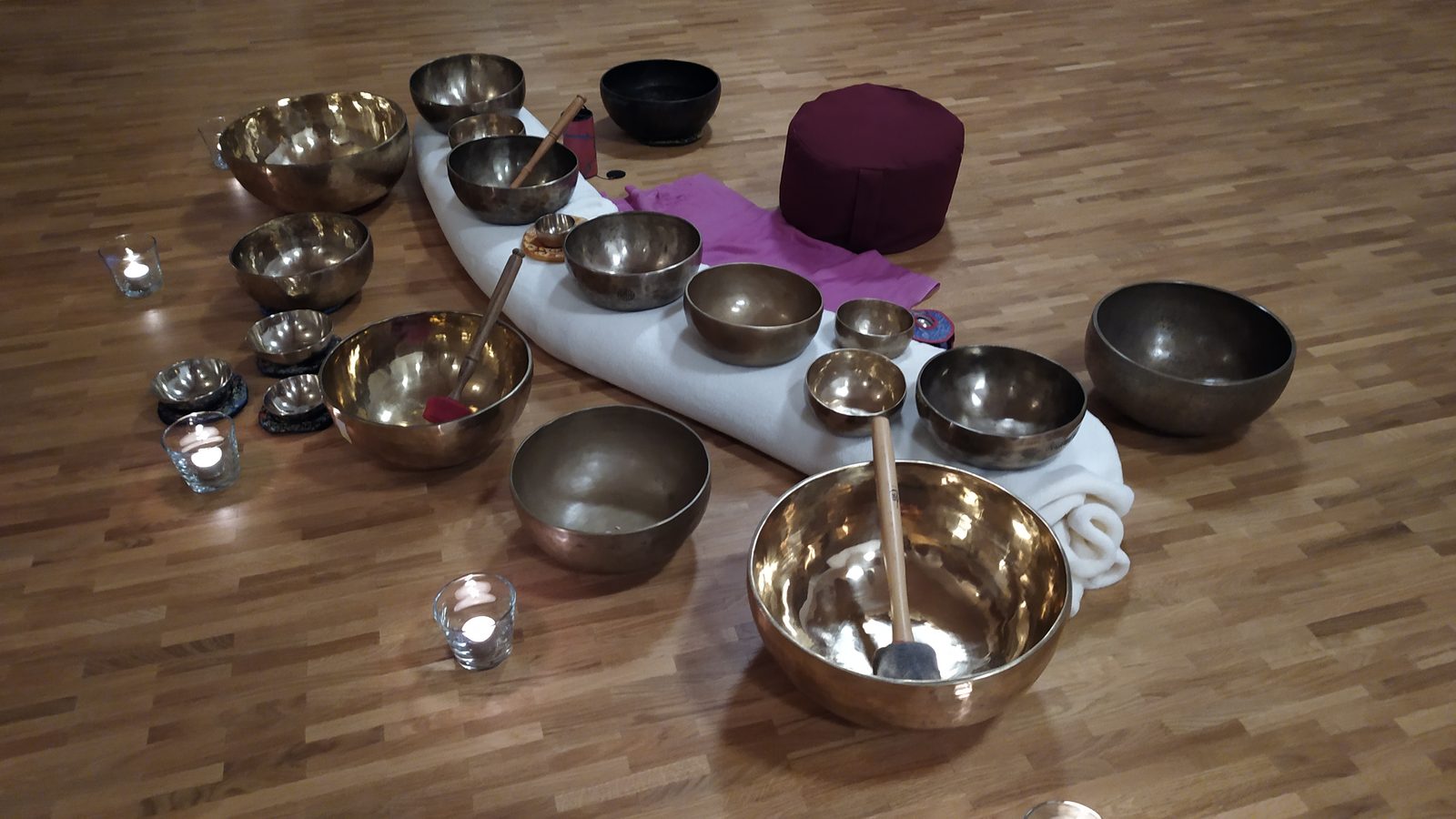 Aufbau des Klangraums – Klangschalen im Halbkreis auf dem Boden, dazwischen Kerzen, Wolldecke und Meditationskissen