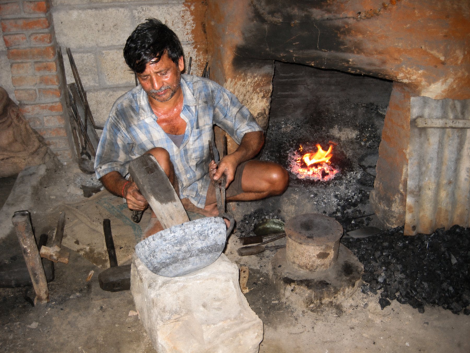Ein Handwerker formt eine glühende Klangschale mit dem Hammer über der Esse – Manufaktur in Nepal